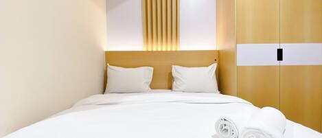 Hotellihuone, jossa on sänky, kaksi tyynyä, puinen vaatekaappi ja sängyllä rullalle taitettu pyyhe.