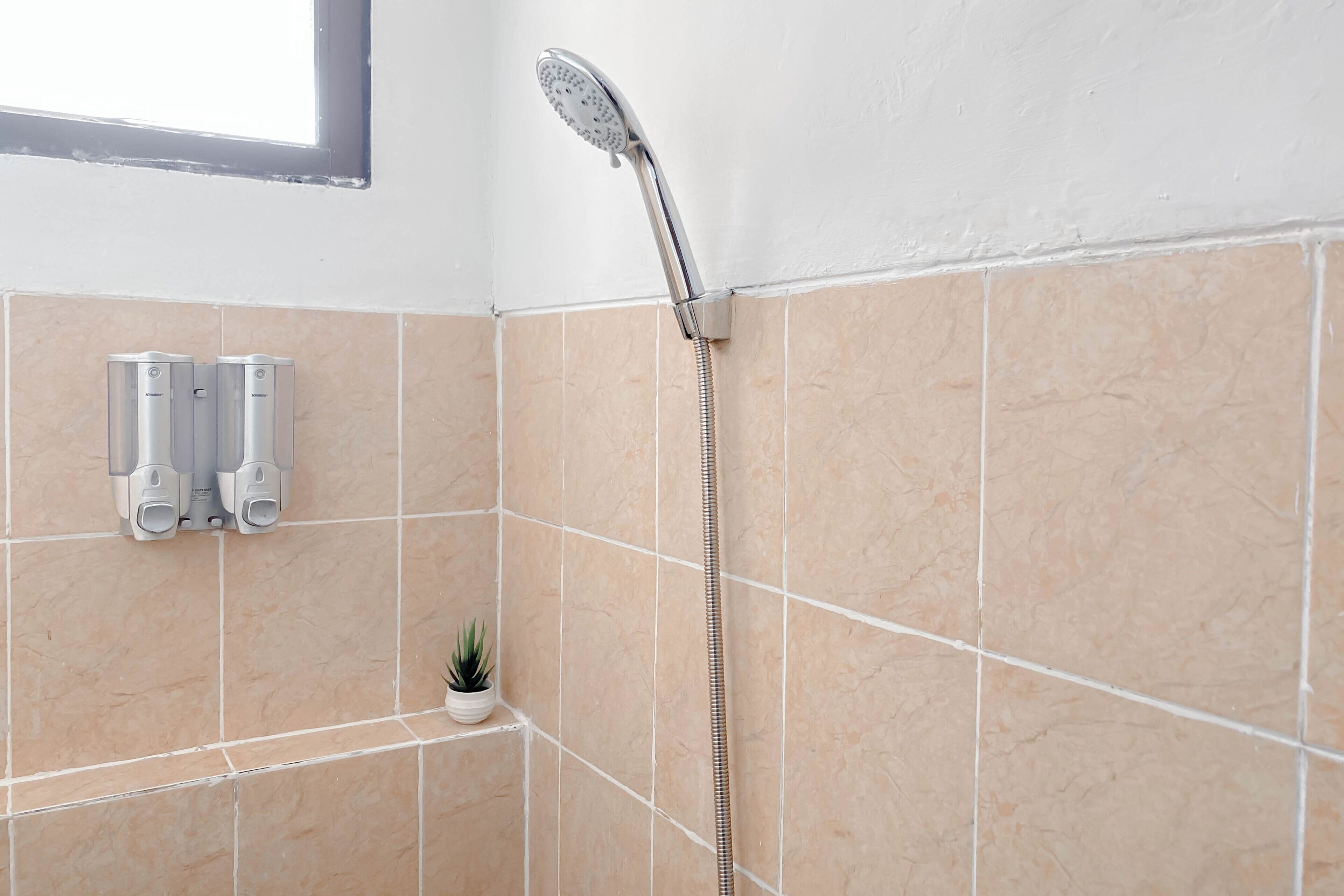A bathroom with beige tiles, a handheld showerhead, and two soap dispensers.