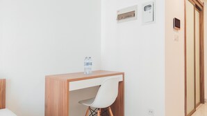 A hotel room with a wooden desk, a white chair, a bed, and a wardrobe. - Restful And Homey Studio At Sky House Alam Sutera Apartment (Tangerang)