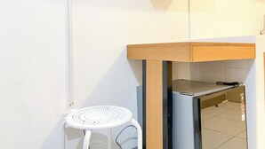 Et kompakt køkken med en lille hvid skammel, indbygget mikroovn og en træbordplade.