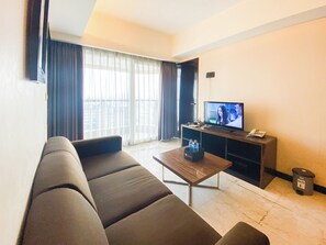 A living room with a sofa, a coffee table, a TV, and a window with curtains.