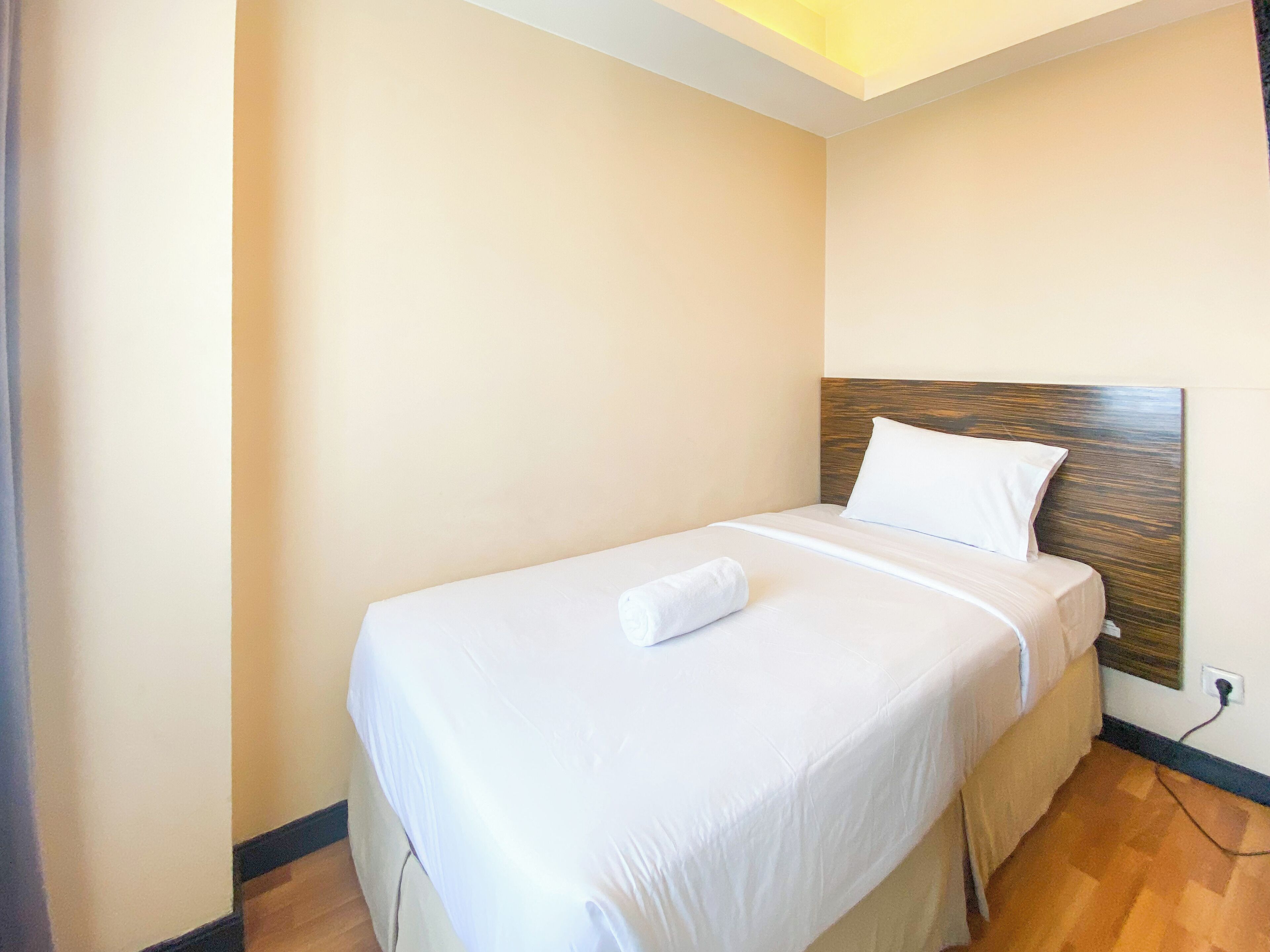 A neatly made bed with white linens and a wooden headboard in a hotel room.