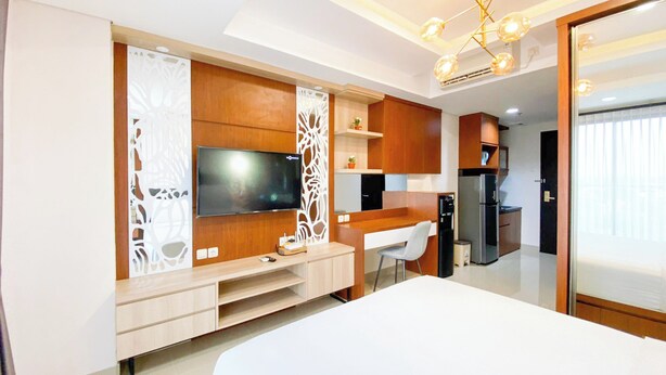 Un dormitorio moderno con una cama grande, un televisor montado en un panel de madera, un escritorio y una zona de kitchenette.
