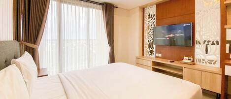 A hotel room with a large bed, a flat-screen TV mounted on the wall, and a desk with a computer.