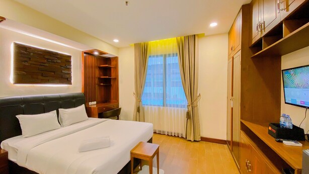 Een hotelkamer met een groot bed, een houten garderobe, een televisie en een raam met gordijnen.