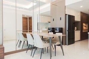 A modern kitchen with a black refrigerator, a built-in oven, and a microwave. There is a dining area with a glass partition and a table with chairs. - Best Spacious And Stylish 3Br At Sky House Bsd Apartment (Pagedangan)