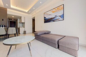 A modern living room with a sofa, a glass-top coffee table, and a painting on the wall. - Best Spacious And Stylish 3Br At Sky House Bsd Apartment (Pagedangan)