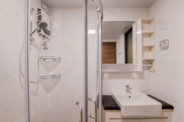 A modern bathroom with a glass shower enclosure, a white sink, and a mirror above the sink. - Best Spacious And Stylish 3Br At Sky House Bsd Apartment (Pagedangan)