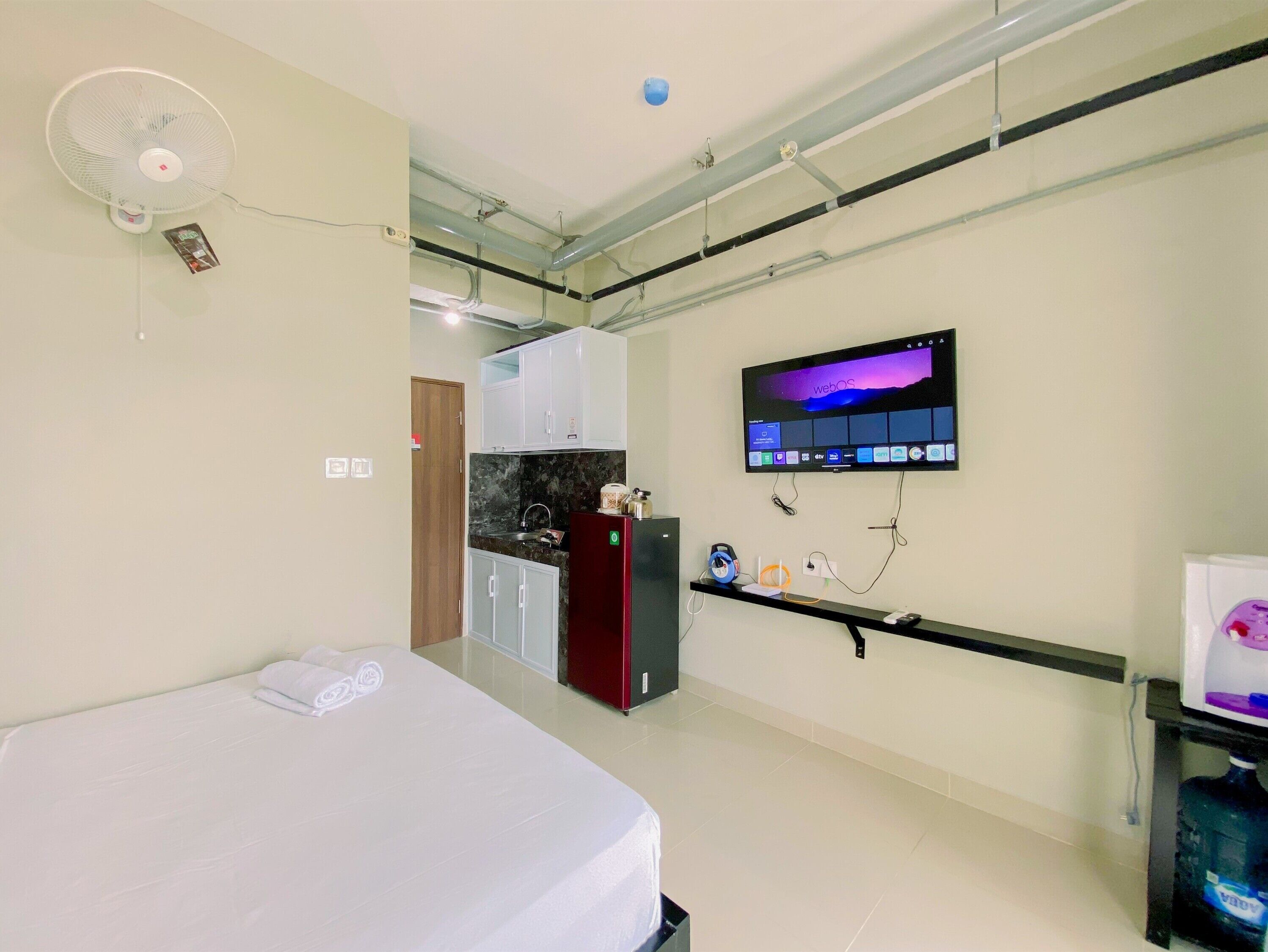 A hotel room with a bed, a desk with a computer, a TV, and a kitchenette.