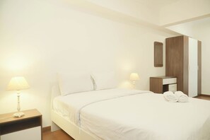 A neatly made bed with white linens, a bedside table with a lamp, and a wooden wardrobe with a mirror. - Good Place 2Br Apartment At Sudirman Tower Condominium (Jakarta)