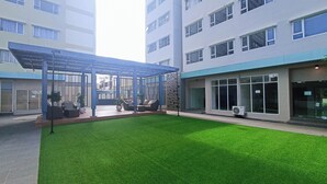 A courtyard with artificial grass, outdoor seating, and a covered area with a pergola. - Cozy 2Br At Royal Makassar Apartment (Makassar)