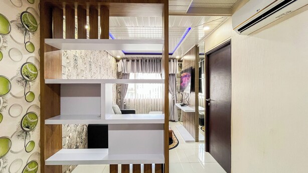 A modern interior with a built-in shelving unit, a television, and a door leading to another room. - Cozy 2Br At Royal Makassar Apartment (Makassar)