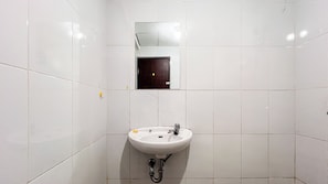 A bathroom with white tiles, a sink, and a mirror. - Cozy 2Br At Royal Makassar Apartment (Makassar)