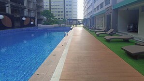 A swimming pool with a wooden deck and lounge chairs, surrounded by high-rise buildings. - Cozy 2Br At Royal Makassar Apartment (Makassar)