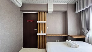 A modern hotel room with a wooden door, a bed with white linens, and built-in shelves. - Cozy 2Br At Royal Makassar Apartment (Makassar)