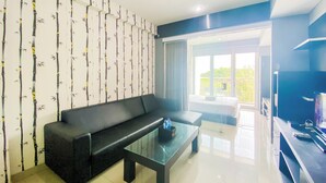 A modern living room with a black sofa, a glass coffee table, and a wall with a bamboo pattern. - Homey 1Br Apartment At Dago Suites (Bandung)