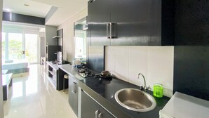 A modern kitchen with black cabinets, a stainless steel sink, and a large window. - Homey 1Br Apartment At Dago Suites (Bandung)