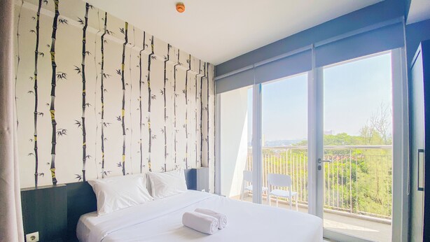 A hotel room with a large bed, a view of the outdoors through a sliding glass door, and a bamboo-themed wall. - Homey 1Br Apartment At Dago Suites (Bandung)