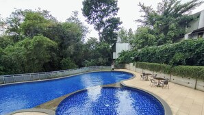 A swimming pool with a tiled deck and a seating area with tables and chairs. - Homey 1Br Apartment At Dago Suites (Bandung)