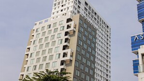 Ein mehrstöckiges Gebäude mit modernem architektonischen Design, das eine Mischung aus rechteckigen und quadratischen Fenstern sowie einen markanten Eckbereich aufweist.