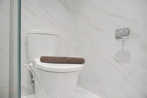Ein modernes Badezimmer mit einer weißen Toilette, Marmorwänden und einer Duschkabine aus Glas.