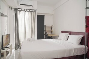 Comfortable accommodations feature a large bed, desk, and chair, along with a television and window with curtains.
