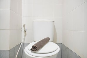 A bathroom with a toilet and towel, featuring a tiled wall and exposed pipes.