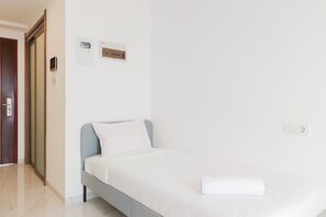 Una camera da letto moderna e pulita con un letto singolo, una porta in legno e una parete bianca con due prese elettriche.