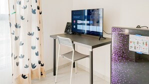 A room with a desk, a chair, a TV, and a refrigerator. - Warm And Homey Studio Apartment At Sky House Alam Sutera (Tangerang)
