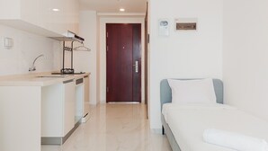 A hotel room with a bed, a small kitchenette, and a door leading to another room. - Warm And Homey Studio Apartment At Sky House Alam Sutera (Tangerang)