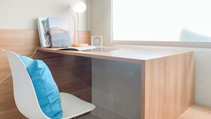 Un espace de travail moderne avec un bureau en bois, un ordinateur portable, un livre intitulé « HYDE AVENUE », une lampe et une chaise dotée d’un coussin bleu.