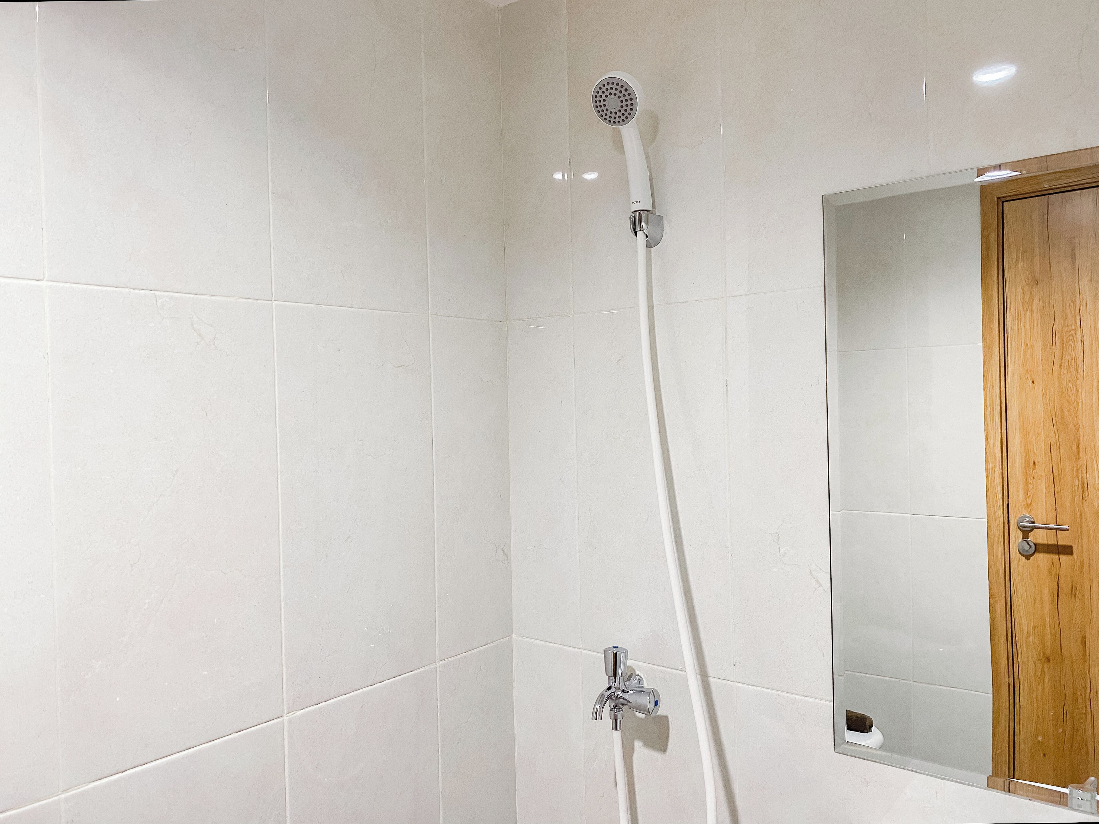 A bathroom with white tiled walls, a wooden door, and a shower with a handheld showerhead.