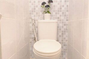 Un inodoro con asiento y tapa blancos, un tanque blanco y una planta en maceta encima.