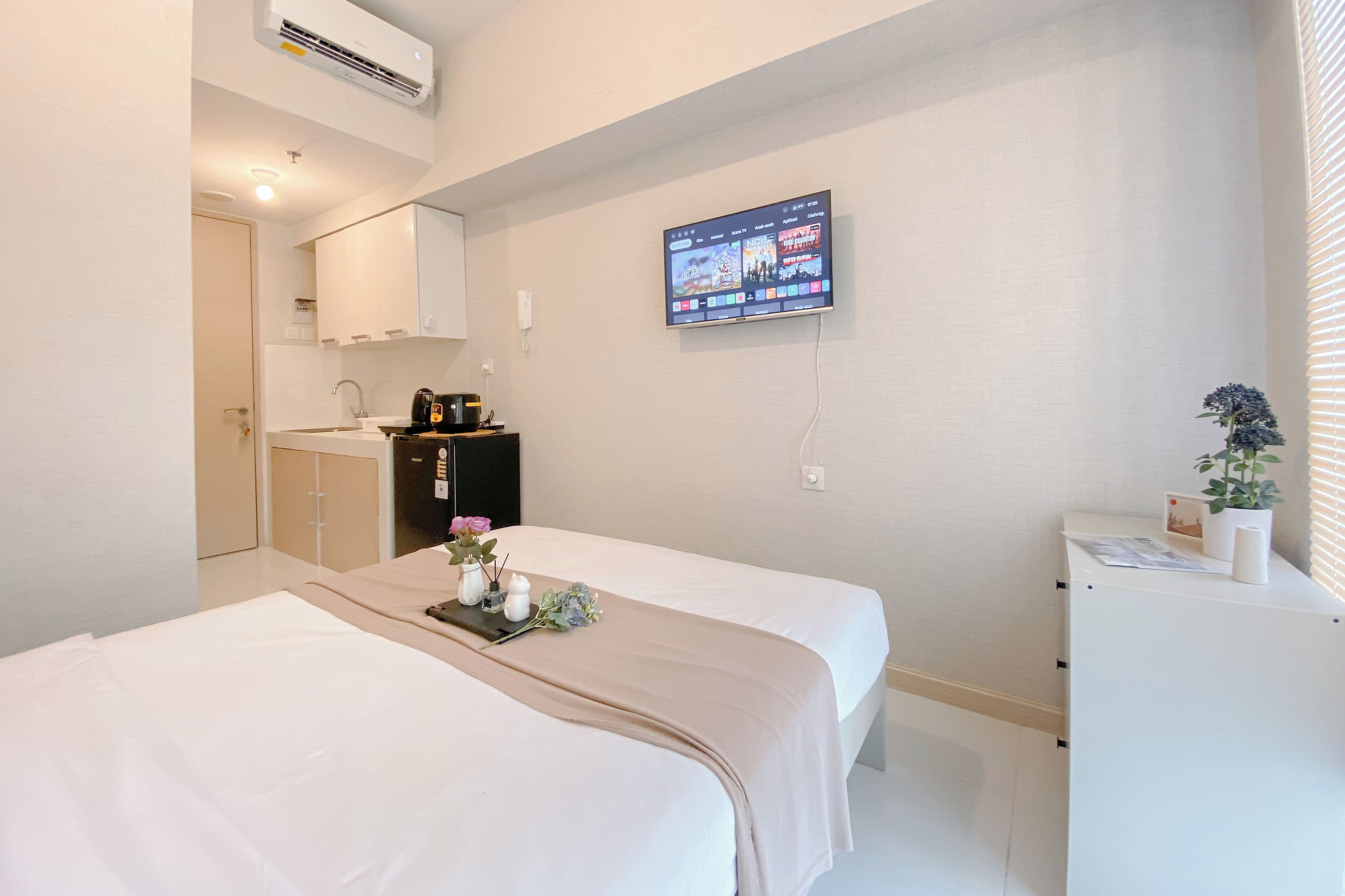 Habitación de hotel con una cama, un escritorio pequeño, un televisor montado en la pared y una ventana con persianas.