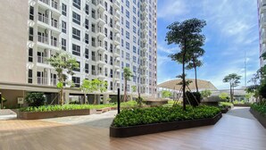 Una plaza urbana moderna con un edificio grande, jardines y cielo despejado.