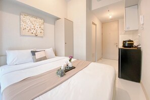 Habitación de hotel con cama, mesita de noche con bandeja, un cuadro en la pared y una zona de kitchenette.