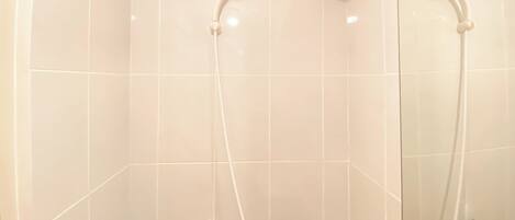 Un baño con azulejos blancos, una ducha con cabezal de ducha manual y un espejo.