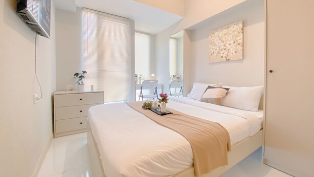 Un dormitorio moderno con una cama grande, una mesita de noche, un espejo y un televisor montado en la pared.