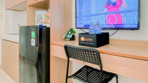 A kitchenette with a refrigerator, a microwave, and a coffee machine. There is a television mounted on the wall displaying a news channel. A black chair is placed in front of the kitchenette. - Cozy And Homey Studio At Springlake Summarecon Bekasi Apartment (Bekasi)