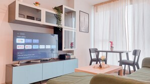 Un salon moderne avec un téléviseur à écran plat, un meuble bleu clair, une table basse en bois et un canapé vert.