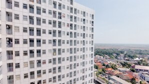 A high-rise building with multiple balconies and a view of a town below. - Homey And Cozy Studio At Serpong Garden Apartment (Cisauk)