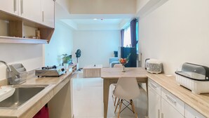 Une cuisine moderne avec un îlot central, un coin repas avec une chaise blanche, et une vue sur un salon avec un canapé et des rideaux.