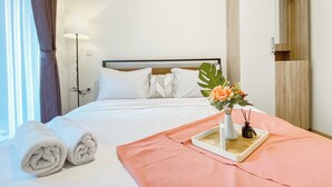 Un lit bien fait, avec des draps blancs, un plaid rose et un plateau sur lequel est posé un vase de fleurs.