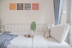 Un letto rifatto con un comofort bianco e cuscini, una pianta sul comodino e una parete con citazioni motivazionali.