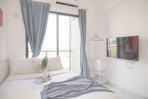 Una camera da letto con un letto, una TV, una finestra con tende e una pianta.