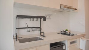 A modern kitchen with a stainless steel sink, a black utensil holder, a stove, and a small potted plant. - Comfy And Best Deal Studio Sky House Bsd Apartment Near Aeon (Pagedangan)