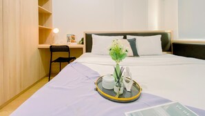 A hotel room with a bed, a desk, a chair, and a small table with a tray. - Modern And Serene Look 2Br Tokyo Riverside Pik 2 Apartment (Teluknaga)