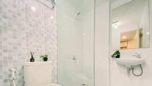 A modern bathroom with a toilet, a glass shower enclosure, and a sink with a mirror. - Modern And Serene Look 2Br Tokyo Riverside Pik 2 Apartment (Teluknaga)