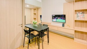 A dining area with a table and chairs, a clock on the wall, and a TV displaying a sports event. - Modern And Serene Look 2Br Tokyo Riverside Pik 2 Apartment (Teluknaga)