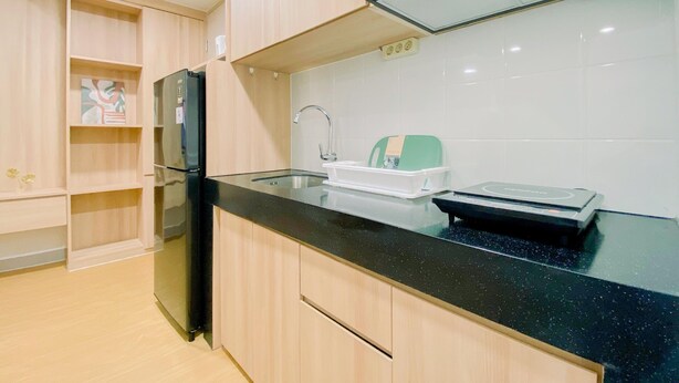 A modern kitchen with light wood cabinets, a black countertop, a built-in oven, and a stainless steel sink. - Modern And Serene Look 2Br Tokyo Riverside Pik 2 Apartment (Teluknaga)